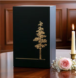 Black Adirondack urn with gold tree design on a wooden table with flowers and a candle.