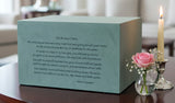 Green Seguin urn with an inscribed poem on a table near a candle and a flower