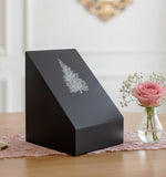 Black slate urn with an inscribed tree set on a table near a vase of pink roses.