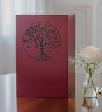 Red painted urn with a tree design on a table near a flower