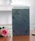 Blank Green slate urn sitting on a table near a pink flower