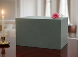 Green Seguin urn with a pink rose on a table with a candle to the left.
